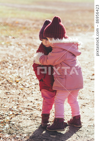 Two children together on the street, hugging, they are sisters or girlfriends. Friendship, family and support concept Two children together on the street, hugging, they are sisters or girlfriends. Friendship, family and support concept 86956423