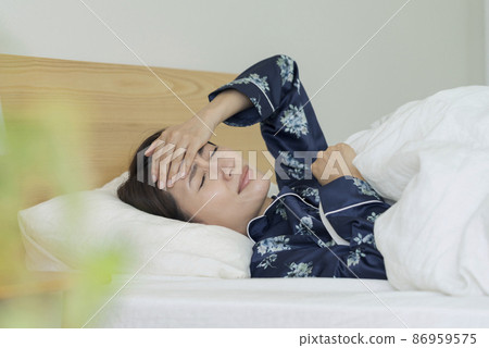 中年婦女睡在床上,雙手放在額頭上 中年婦女睡在床上,雙手放在額頭上 86959575