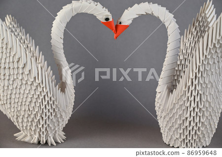 A pair of origami swans against a gray background. 86959648