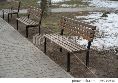 Three empty park benches in a spring park. Melting snow on the lawn in the background. No people. Daytime. Selective focus. 86959650