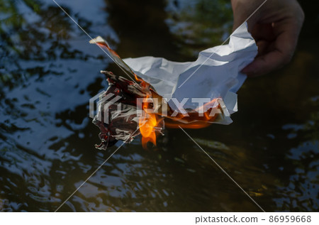 A wrinkled piece of paper burning in a man's hand.  86959668