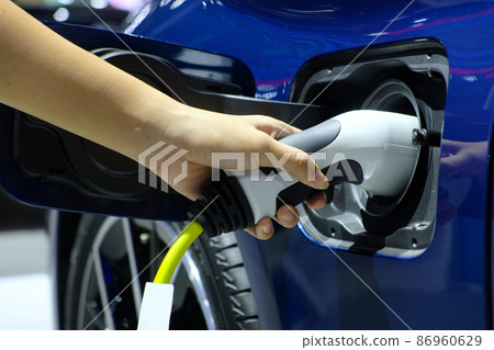 Close-up hand woman who holding electric charge machine for rechargeable battery with blue electric car, Zero Emission Vehicle (ZEV), Battery Electric Vehicle (BEV), Hybrid Electricity Vehicle (HEV) 86960629