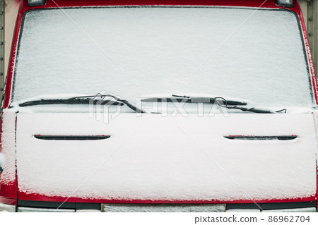 The windshield of the car covered with snow. Windscreen wipers are like eyebrows above the eyes. The windshield of the car covered with snow. Windscreen wipers are like eyebrows above the eyes. 86962704