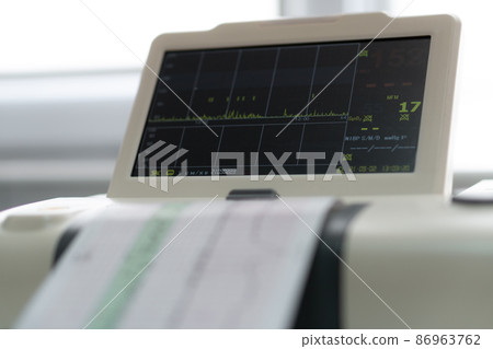 Electronic Cardiotocography Machine Monitoring Fetal Heart Contractions Of Uterus. Printing Cardiogram Report Coming Out Electrocardiogram In Labor Ward During Pregnancy. Medical Diagnostic Equipment 86963762