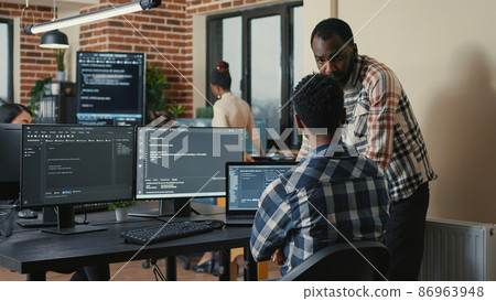Software developer writing code on laptop and computer keyboard looking at multiple screens Software developer writing code on laptop and computer keyboard looking at multiple screens 86963948