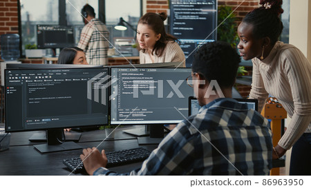 Mixed team of artificial intelligence cloud programers talking about programming in front of multiple screens 86963950