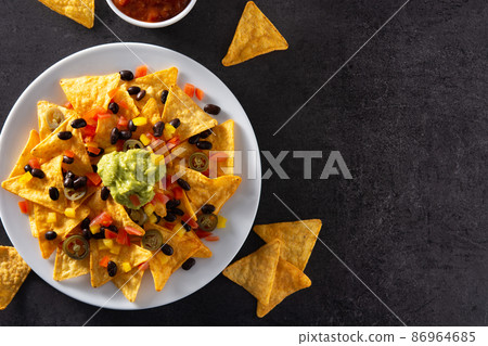 Mexican nachos tortilla chips with black beans, guacamole, tomato and jalapeno 86964685