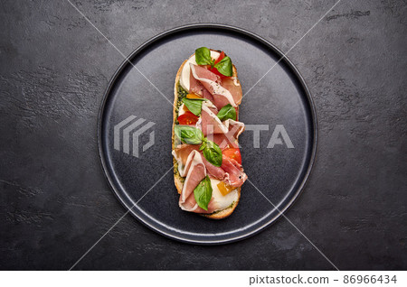 Flat lay bruschetta with mozzarella, Parma ham and pesto on black plate Flat lay bruschetta with mozzarella, Parma ham and pesto on black plate 86966434