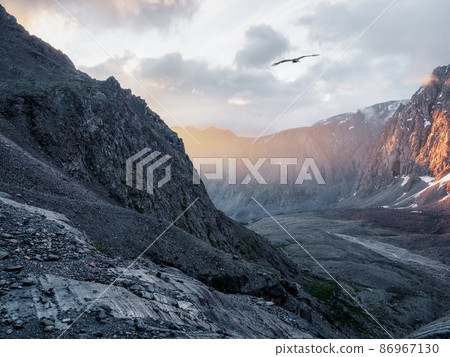 Mountain valley at sunrise. Awesome mountain valley view from cliff at very high altitude in sunrise.  Beautiful mountain scenery on abyss edge with sharp stones. 86967130