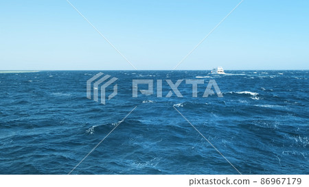 Azure sea with waves on sunny windy day. White cruise yacht sailing blue Red sea surface, view of moving boat. Yachting tour in Egypt blue sky above horizon. Natural marine background. Nautical voyage Azure sea with waves on sunny windy day. White cruise yacht sailing blue Red sea surface, view of moving boat. Yachting tour in Egypt blue sky above horizon. Natural marine background. Nautical voyage 86967179