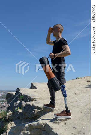 a man on a prosthetic leg travels the mountains. Dressed in black jeans and a T-shirt, he carrying mat 86967443