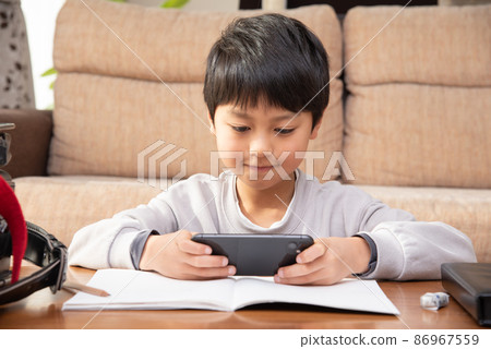 Elementary school boy playing online games on his smartphone after his homework 86967559
