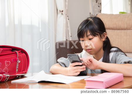 Elementary school girl looking at a smartphone while studying 86967560