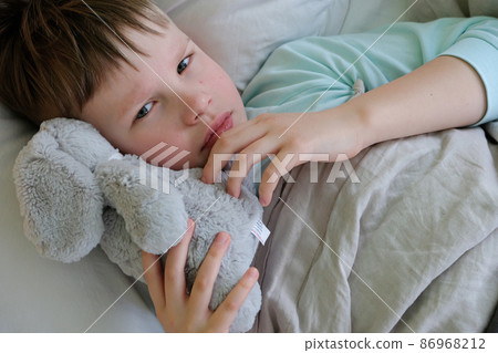 The child is lying with a fever in bed with a plush toy The child is lying with a fever in bed with a plush toy 86968212