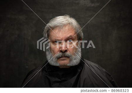Dramatic portrait of emotional senior bearded man getting beard grooming isolated on dark vintage background. Concept of emotions, fashion, beauty, self-reinvention 86968323