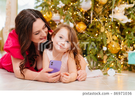 mother and daughter under the Christmas tree with a smartphone. mother and daughter under the Christmas tree with a smartphone. 86971036