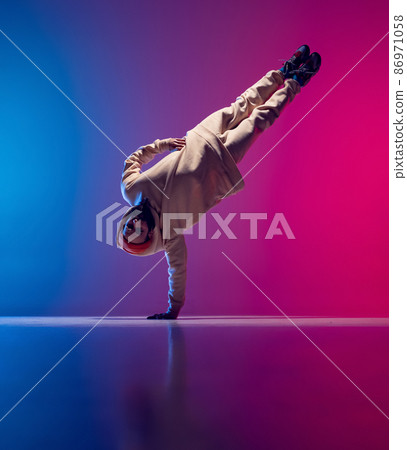 Studio shot of young flexible sportive man dancing breakdance in white outfit on gradient pink blue background. Concept of action, art, beauty, sport, youth 86971058