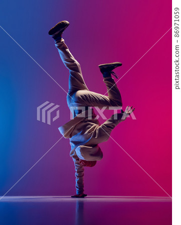 Studio shot of young flexible sportive man dancing breakdance in white outfit on gradient pink blue background. Concept of action, art, beauty, sport, youth 86971059