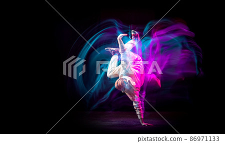 Dynamic portrait of young flexible sportive boy dancing hip-hop or breakdance in white outfit on dark background in mixed pink neon light. Sport, art, action, moves 86971133