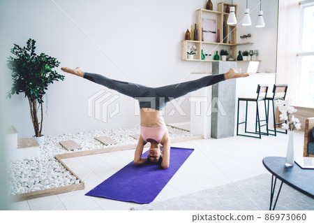 Caucasian female athlete dressed in tracksuit trains hard in home interior practice body balance 86973060