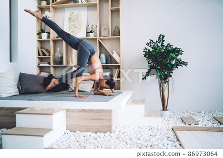 Young slim brunette doing difficult arm standing asana during yoga training Young slim brunette doing difficult arm standing asana during yoga training 86973064