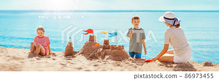 Mother with son and daughter sitting on the beach and building a sand castle. Mother with son and daughter sitting on the beach and building a sand castle. 86973455