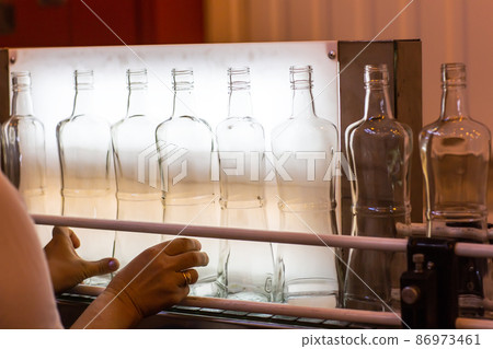 Small liquor production based on maple syrup. Lot of pure alcohol bottles unlabeled. Bottles placed in a row. Person in lab coat analyzing the bottles 86973461