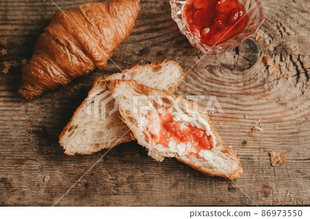 cut croissant with butter and strawberry jam , on a wooden background, top view. Sweet and hearty breakfast with croissants. 86973550