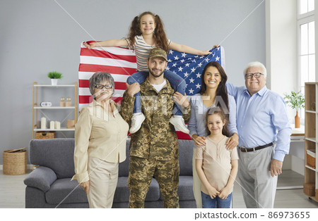 Portrait of a military father and his big happy family with an American flag in his hands. Grandparents, soldier's wife and daughters looking at the camera smiling. Concept of military service. Portrait of a military father and his big happy family with an American flag in his hands. Grandparents, soldier's wife and daughters looking at the camera smiling. Concept of military service. 86973655