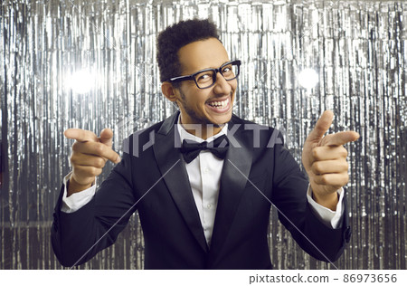 You are chosen for this. Cheerful man makes finger guns gesture directly at camera standing on shiny silver background. Smiling young dark skinned man in black classic suit pointing his fingers at you You are chosen for this. Cheerful man makes finger guns gesture directly at camera standing on shiny silver background. Smiling young dark skinned man in black classic suit pointing his fingers at you 86973656