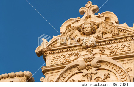 Lecce, Puglia, Italy. August 2021. The church of Santa Croce is the finest example of Lecce baroque. Detail of the facade illuminated by the warm light of the evening. 86973811