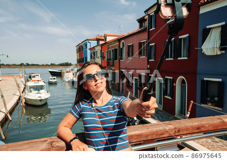 Influence media Burano Italy. Paint building house in Europe Venezia city. Travel photographer blogger girl with smartphone in Venice island color street. Freedom, summer travel, profession concept. 86975645