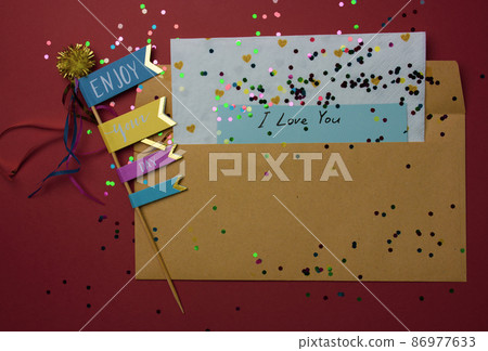 Love letter. A brown envelope with a Valentine's Day declaration of love note on a terra cotta background. Scattered colorful confetti, flags, heart. Festive greeting card for February 14 top view. Love letter. A brown envelope with a Valentine's Day declaration of love note on a terra cotta background. Scattered colorful confetti, flags, heart. Festive greeting card for February 14 top view. 86977633