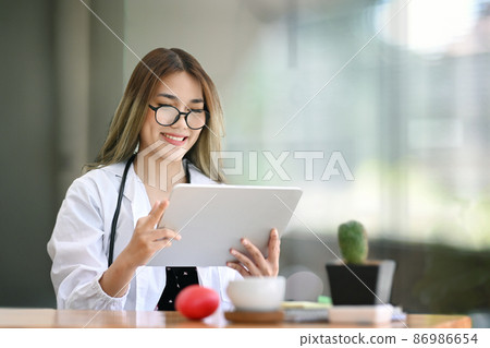 Smiling female doctor using digital tablet in bright modern hospital. Smiling female doctor using digital tablet in bright modern hospital. 86986654
