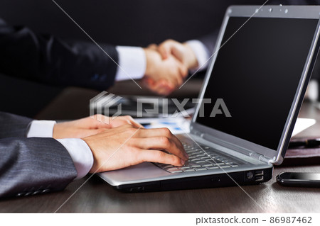Close up of businessman's hand working with laptop on the background of a business handshake Close up of businessman's hand working with laptop on the background of a business handshake 86987462