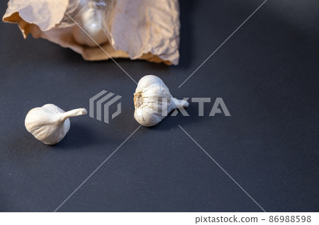 Brown paper bag with garlic against a black background. Heads of ripe garlic in the peel. Close-up. Selective focus Brown paper bag with garlic against a black background. Heads of ripe garlic in the peel. Close-up. Selective focus 86988598