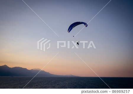 Silhouette of a man on a paraglider flying over the sea at sunset. 86989257