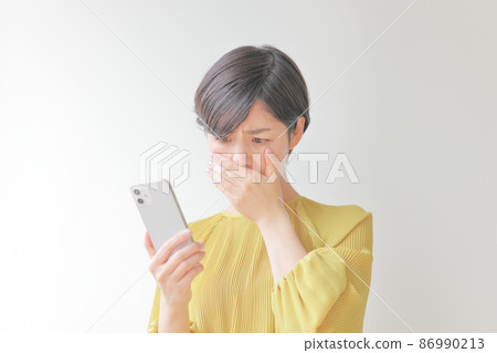 A woman with a sad expression who puts her hand on her mouth and stares at her smartphone 2 A woman with a sad expression who puts her hand on her mouth and stares at her smartphone 2 86990213