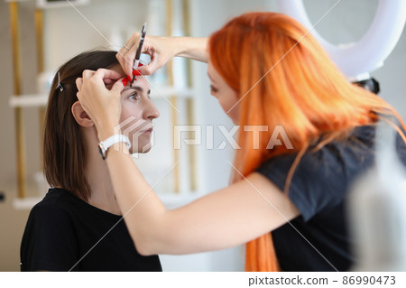 Master draws eyebrows to a woman with a pencil Master draws eyebrows to a woman with a pencil 86990473