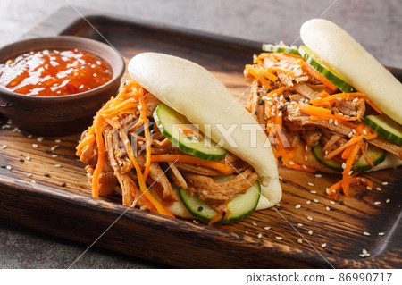Delicious steamed bao buns sandwiches with pulled pork close-up on a wooden tray. horizontal Delicious steamed bao buns sandwiches with pulled pork close-up on a wooden tray. horizontal 86990717
