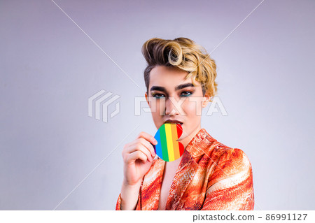 non binary portrait of asian man with luxurious blonde hair and gorgeous make-up in white wall studio background passion look with rainbow heart on mouth 86991127