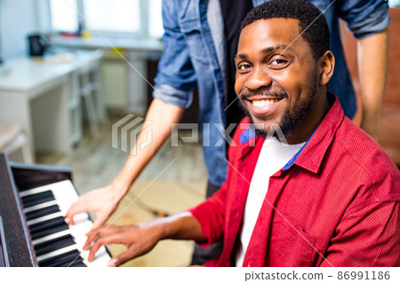 latin hispanic man learning to play on piano with caucasian teacher in classroom latin hispanic man learning to play on piano with caucasian teacher in classroom 86991186