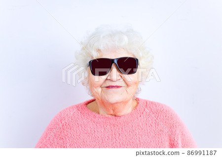 Portrait of funny senior blonde woman in sun glasses and pink sweater on white background 86991187
