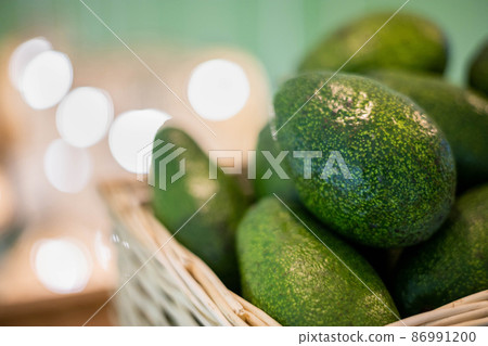 Organic farm avocado in straw basket on wooden table closeup. Fresh ripe green exotic fruits Organic farm avocado in straw basket on wooden table closeup. Fresh ripe green exotic fruits 86991200