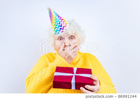 older woman with a gift wear yellow sweater and horn cap on a white background 86991244