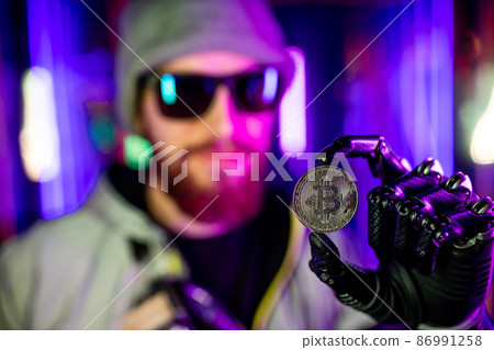 man with prosthetic robot hand holding bit-coin golden in neon background 86991258