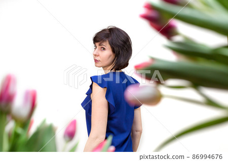 A brunette woman 35-40 years old in a blue blouse against the background of spring tulips. isolated, white background A brunette woman 35-40 years old in a blue blouse against the background of spring tulips. isolated, white background 86994676