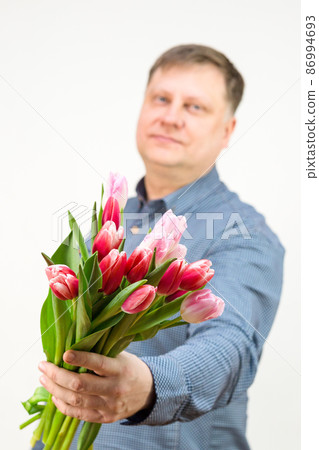 An adult male blonde holds out a bouquet of bright fragrant tulips, isolated, white background, out of focus, blurry An adult male blonde holds out a bouquet of bright fragrant tulips, isolated, white background, out of focus, blurry 86994693