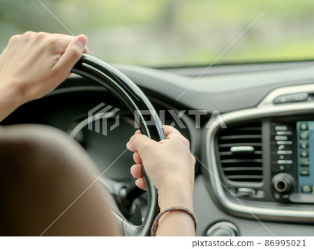 Female hands on the black glossy steering wheel of a car.. Driving a car. Soft focus Female hands on the black glossy steering wheel of a car.. Driving a car. Soft focus 86995021