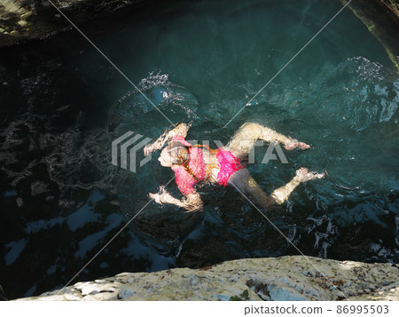 A girl swims in a frog pose in a turquoise river lit by the sun 86995503